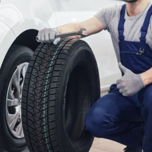 Mann hält neuen Reifen vor einem Auto